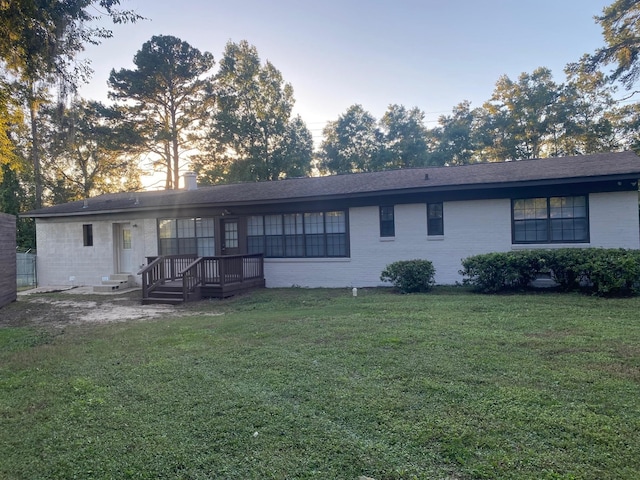 back house at dusk with a deck and a lawn