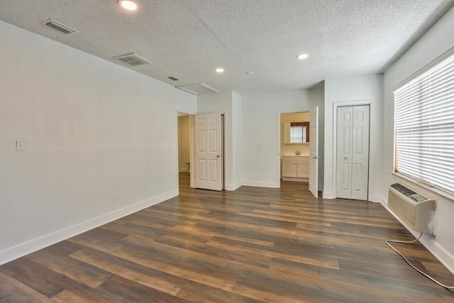 empty room with an AC wall unit, a textured ceiling, and dark hardwood / wood-style floors