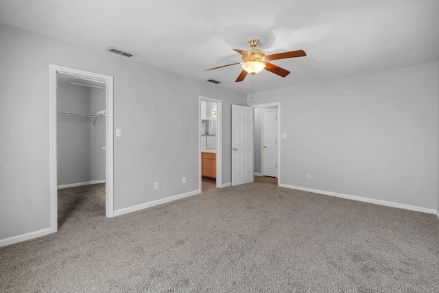 unfurnished bedroom with a closet, a spacious closet, connected bathroom, ceiling fan, and light colored carpet