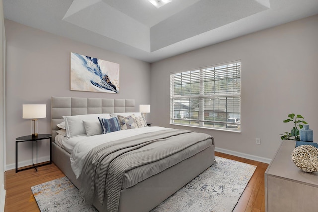 bedroom with light hardwood / wood-style flooring and a tray ceiling