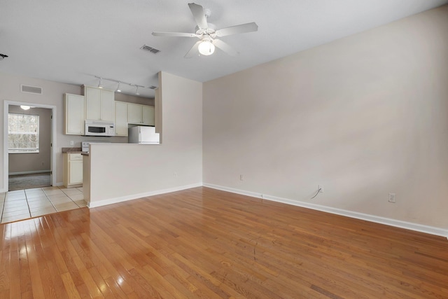 unfurnished living room featuring rail lighting, ceiling fan, and light hardwood / wood-style flooring