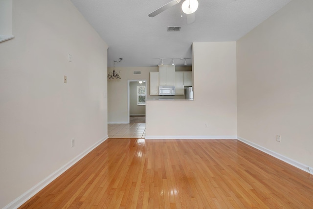 unfurnished living room featuring rail lighting, ceiling fan, light wood-type flooring, and a textured ceiling