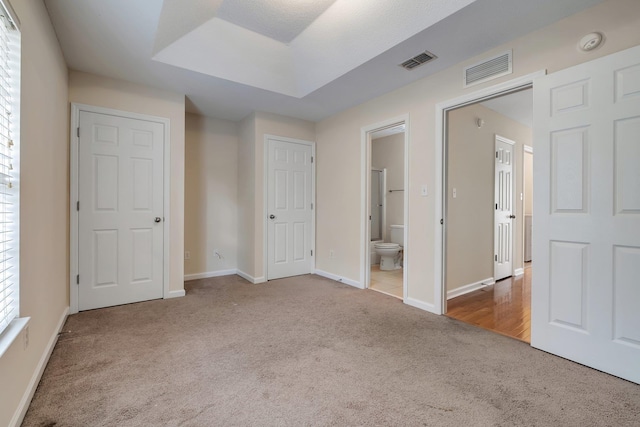 unfurnished bedroom with ensuite bathroom and light colored carpet