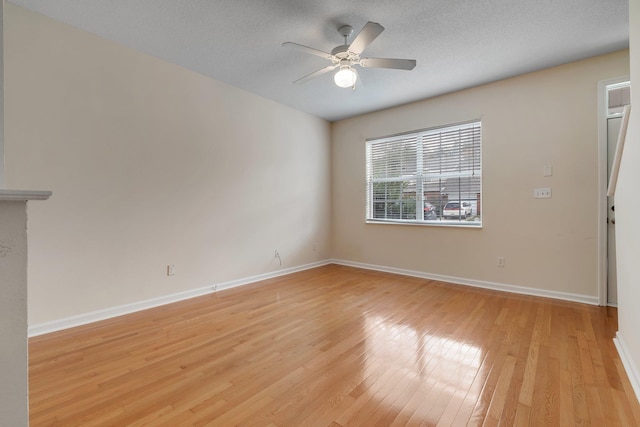 empty room with ceiling fan, light wood-type flooring, and a textured ceiling