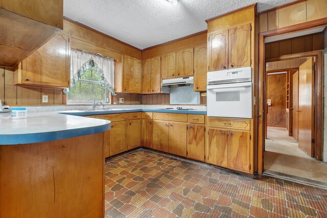 6206 Blountstown Hwy, Tallahassee, FL 32310 - kitchen with white appliances, under cabinet range hood, light countertops, brown cabinetry, and a textured ceiling