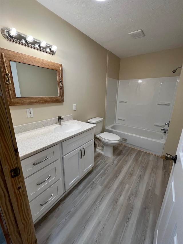 full bathroom with vanity, wood-type flooring, a textured ceiling, and toilet