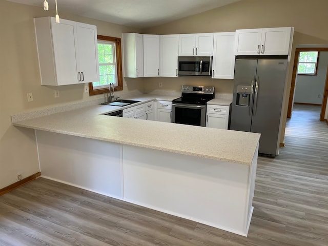 kitchen with stainless steel appliances, vaulted ceiling, kitchen peninsula, sink, and white cabinetry