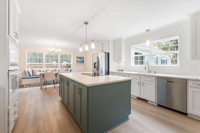 kitchen with white cabinetry, hanging light fixtures, a kitchen island, and appliances with stainless steel finishes