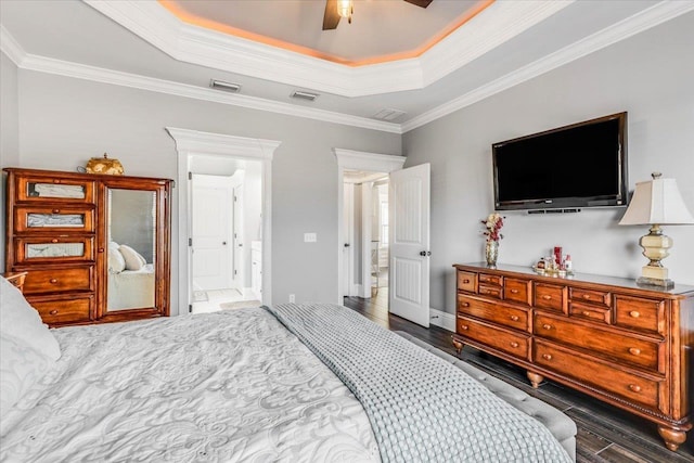 bedroom with a tray ceiling, wood finished floors, visible vents, and crown molding