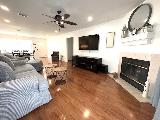 living room with ceiling fan, a tile fireplace, recessed lighting, wood finished floors, and visible vents