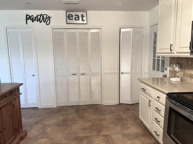 kitchen featuring light countertops, backsplash, stone finish flooring, white cabinets, and stainless steel range with electric cooktop