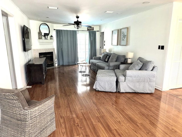 living room with a tiled fireplace, a ceiling fan, and dark wood-style flooring