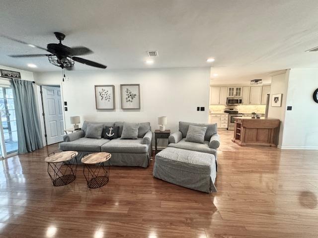 living area featuring a ceiling fan, light wood-type flooring, visible vents, and baseboards