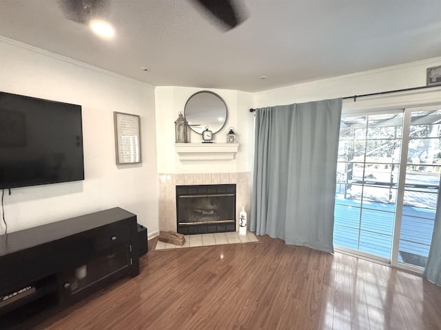 living area featuring crown molding, a tiled fireplace, and wood finished floors