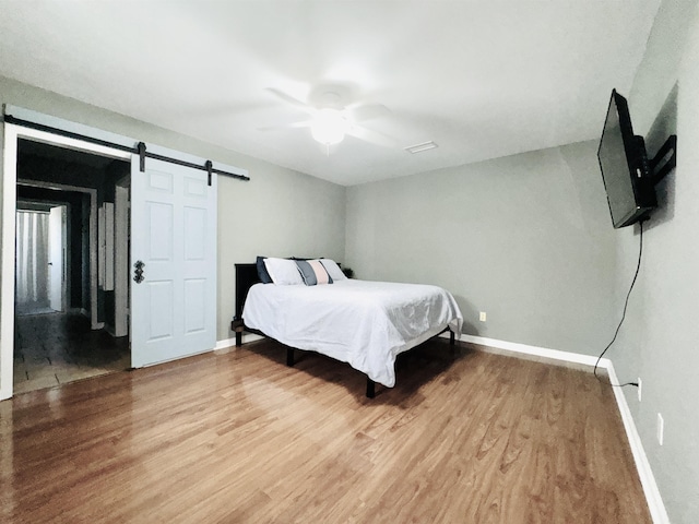 bedroom featuring baseboards, ceiling fan, light wood finished floors, and a barn door