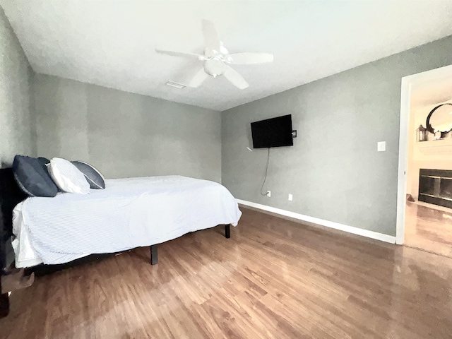 bedroom featuring a ceiling fan, a fireplace, baseboards, and wood finished floors