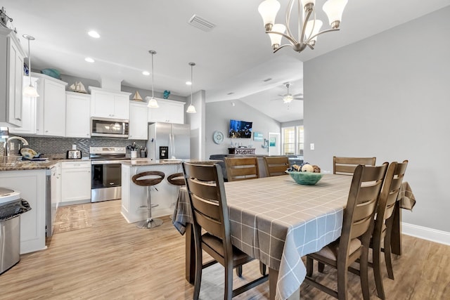 dining space featuring ceiling fan with notable chandelier, light hardwood / wood-style floors, and lofted ceiling