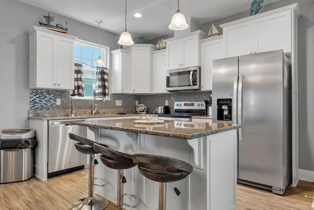 kitchen with pendant lighting, a center island, dark stone countertops, white cabinetry, and stainless steel appliances