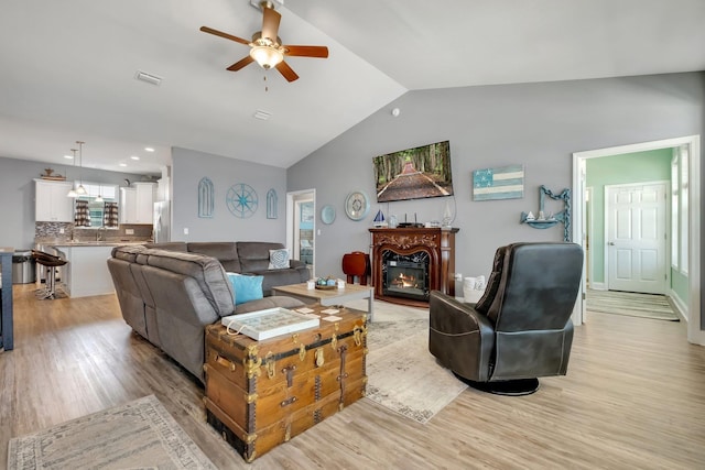 living room with light hardwood / wood-style floors, vaulted ceiling, ceiling fan, and sink