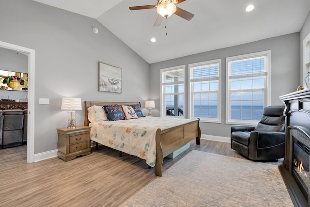 bedroom featuring ceiling fan, light hardwood / wood-style flooring, a water view, and vaulted ceiling