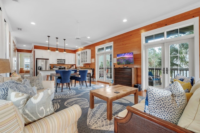 living room with light hardwood / wood-style floors, french doors, wooden walls, and ornamental molding