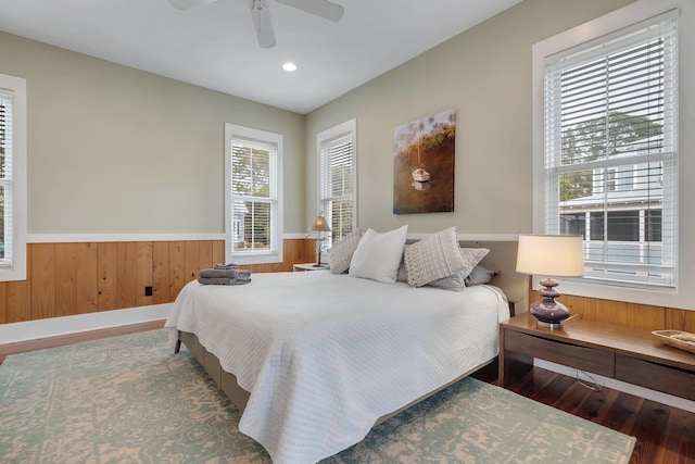 bedroom with ceiling fan, wood-type flooring, and wooden walls