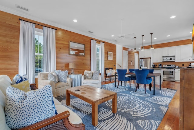 living room with crown molding, wood walls, ceiling fan, and wood-type flooring