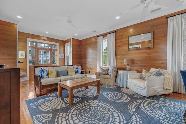 living room with wood walls, ceiling fan, crown molding, and wood-type flooring