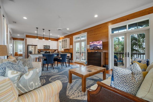 living room featuring ornamental molding, french doors, wooden walls, and light hardwood / wood-style flooring