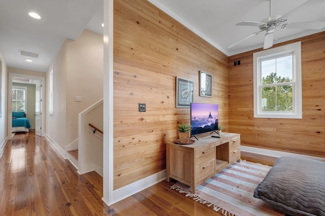 bedroom with wood walls, ceiling fan, and wood-type flooring