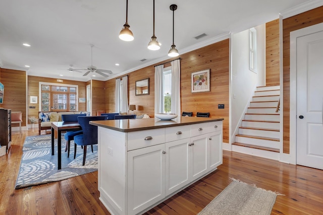 kitchen featuring light hardwood / wood-style flooring, hanging light fixtures, white cabinets, wood walls, and a center island