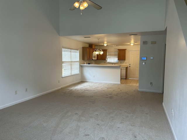 unfurnished living room with ceiling fan with notable chandelier, a towering ceiling, and light carpet