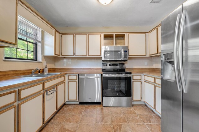 1541 San Luis Rd, Tallahassee, FL 32304 - kitchen featuring cream cabinets, a sink, stone finish flooring, backsplash, and stainless steel appliances
