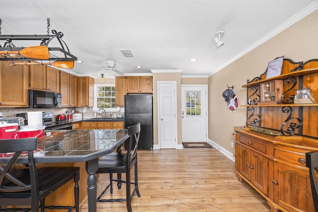 kitchen with backsplash, tile counters, a breakfast bar, black appliances, and a sink