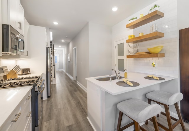 kitchen with a breakfast bar, kitchen peninsula, stainless steel appliances, decorative backsplash, and white cabinets