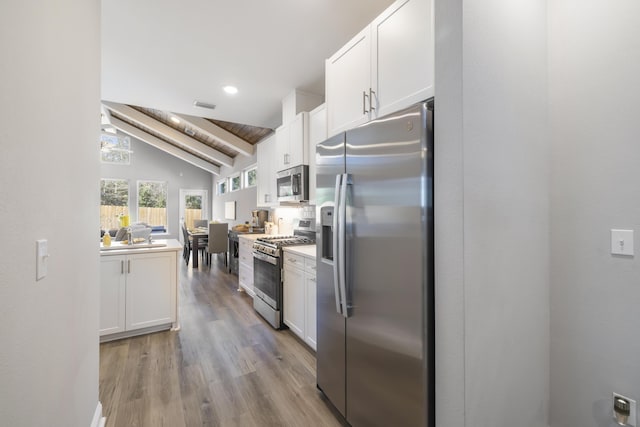 kitchen with white cabinetry, vaulted ceiling with beams, light hardwood / wood-style flooring, and stainless steel appliances