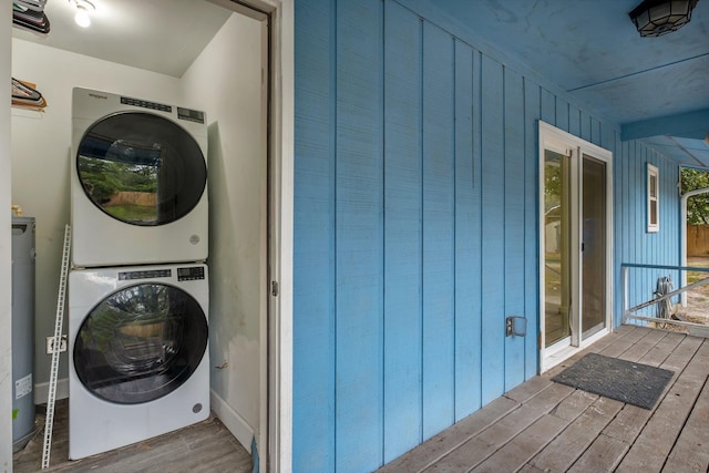 washroom with stacked washing maching and dryer, wood-type flooring, wooden walls, and gas water heater