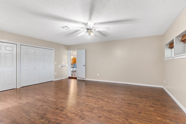 unfurnished bedroom featuring dark hardwood / wood-style flooring, two closets, and a textured ceiling