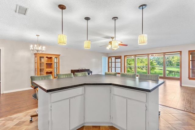 kitchen featuring a kitchen island, ceiling fan with notable chandelier, pendant lighting, white cabinets, and a textured ceiling