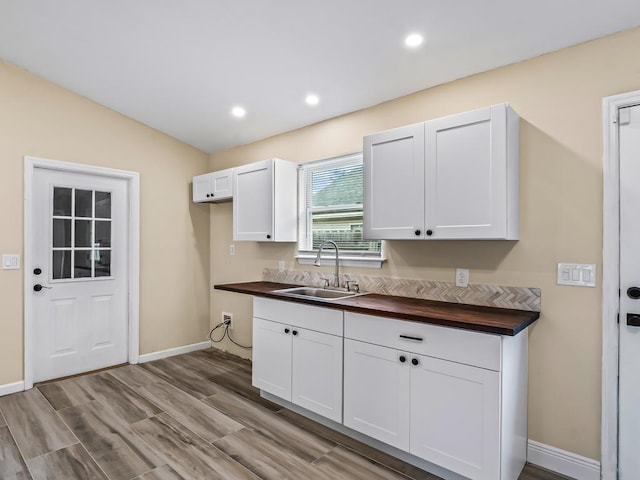 kitchen with light wood-type flooring, butcher block countertops, white cabinetry, and sink