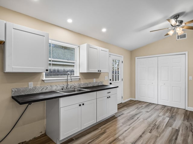 kitchen with sink, white cabinets, vaulted ceiling, and light wood-type flooring