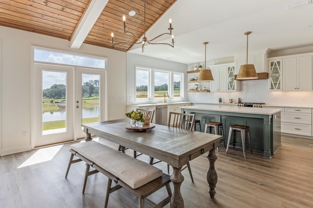 dining room with french doors, a water view, light wood-style flooring, lofted ceiling with beams, and wood ceiling