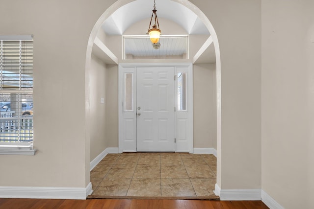 foyer with arched walkways, baseboards, and wood finished floors