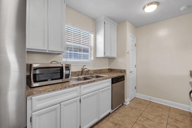 kitchen with appliances with stainless steel finishes, dark countertops, a sink, and white cabinets