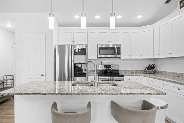 kitchen with stainless steel appliances, sink, a kitchen island with sink, white cabinets, and pendant lighting