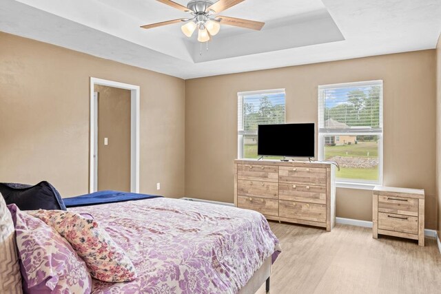 bedroom featuring ceiling fan, light wood-type flooring, and a tray ceiling