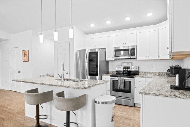 kitchen with appliances with stainless steel finishes, an island with sink, light hardwood / wood-style floors, and white cabinets