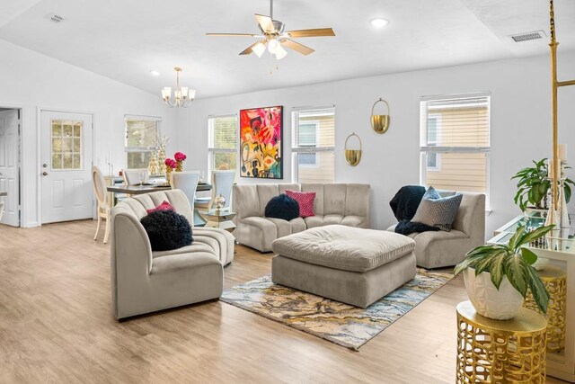 living room with ceiling fan with notable chandelier, light hardwood / wood-style floors, and vaulted ceiling