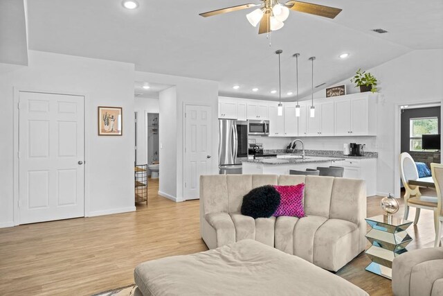 living room featuring light wood-type flooring, ceiling fan, sink, and vaulted ceiling