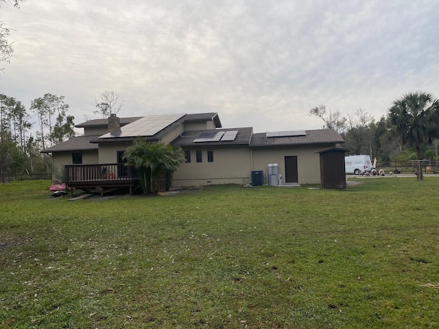 rear view of house with solar panels, central air condition unit, a lawn, and a wooden deck